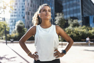 Thoughtful young woman wearing sports bra while listening music against  buildings in city stock photo