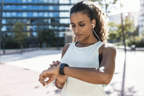 Junge Frau stellt an einem sonnigen Tag eine intelligente Uhr ein - JSRF02288