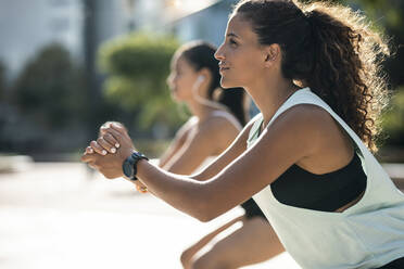 Smiling young woman with friend exercising on sunny day - JSRF02297