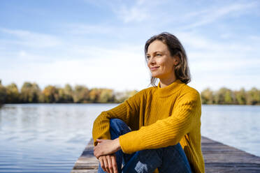 Thoughtful woman sitting on jetty under sky - DIGF19287