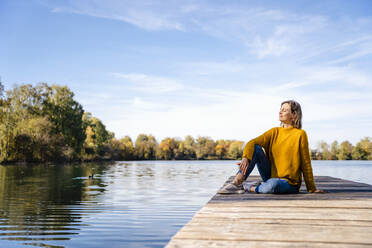 Woman sitting on jetty in front of lake - DIGF19290