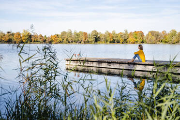 Frau sitzt auf Steg am See - DIGF19296