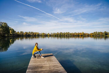 Frau sitzt auf Klampe vor See unter Himmel - DIGF19301