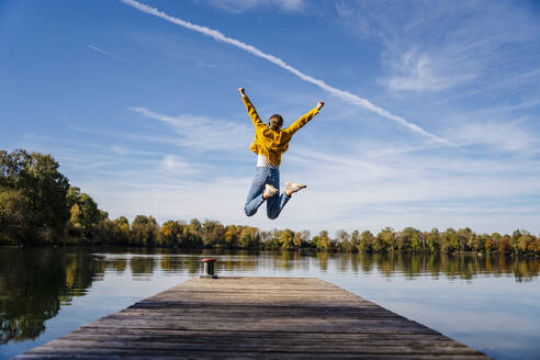 Carefree woman jumping on jetty under vapor trail - DIGF19303