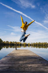 Woman with arms raised jumping on jetty under sky - DIGF19305