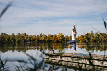 Frau übt Yoga vor einem See an einem sonnigen Tag - DIGF19329