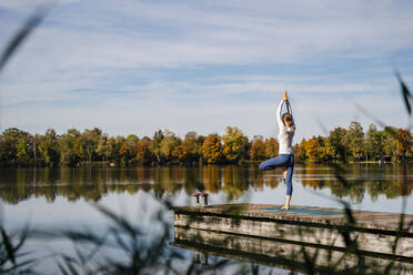 Woman practicing yoga in front of lake on sunny day - DIGF19329