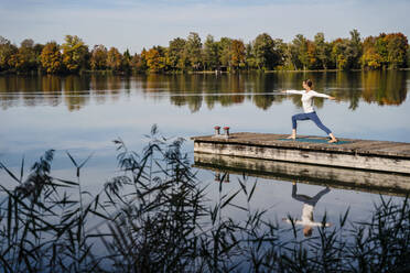 Woman with arms outstretched practicing yoga on jetty - DIGF19330