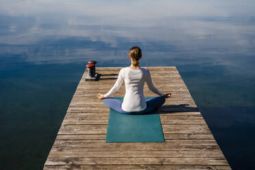 Woman meditating at jetty on sunny day - DIGF19339