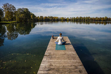 Woman meditating in front of lake under sky - DIGF19340