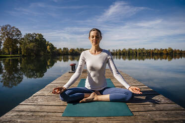 Frau mit geschlossenen Augen praktiziert Meditation vor einem See - DIGF19342