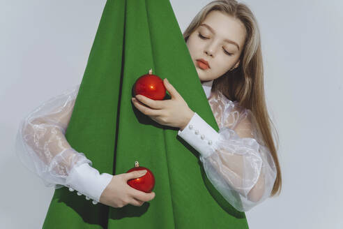 Girl holding red baubles embracing abstract Christmas tree against white background - IEF00221