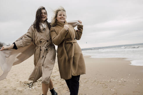 Mother and daughter wearing overcoats having fun at beach - VIVF00184