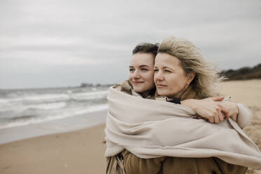 Mother and daughter wrapped in blanket at beach - VIVF00186