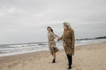 Mutter und Tochter halten sich an den Händen am Strand - VIVF00189