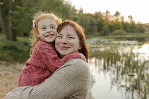 Smiling girl embracing grandmother near lake - VIVF00221