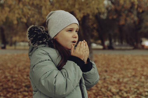 Mädchen mit Strickmütze wärmt sich im Herbst im Park die Hände - JBUF00127