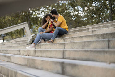 Glückliches junges Paar sitzt auf einer Treppe und verbringt seine Freizeit miteinander - JCCMF07946