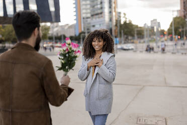 Young man giving bouquet of flowers to woman at footpath - JCCMF07962