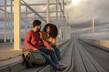 Lächelnde Frau mit Mann auf Stufen sitzend bei Sonnenuntergang - JCCMF07985