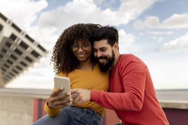 Glückliches junges Paar mit Smartphone unter bewölktem Himmel - JCCMF08009