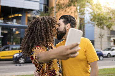 Junges Paar, das sich küsst und ein Selfie mit dem Smartphone auf dem Fußweg macht - JCCMF08032