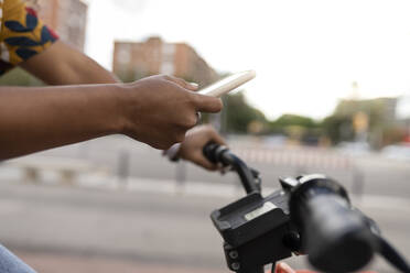 Hand einer Frau, die ein Smartphone benutzt und auf einem Fußweg Fahrrad fährt - JCCMF08037