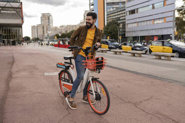 Happy young man riding bicycle at footpath - JCCMF08041