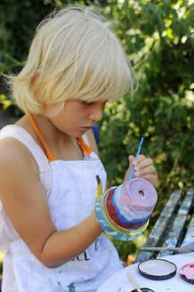 Little girl painting flower pots in garden - GISF00942