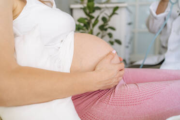 Hand einer schwangeren Frau, die ihren Bauch berührt, sitzt zu Hause auf dem Bett - MDOF00202