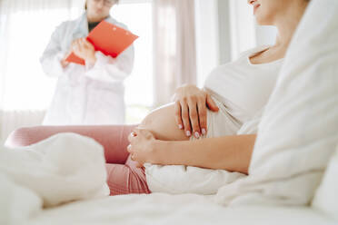 Schwangere Frau berührt Bauch auf dem Bett liegend zu Hause - MDOF00211