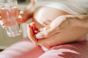 Schwangere Frau hält Tabletten und Trinkwasser in der Hand - MDOF00213