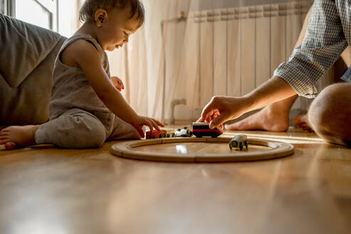 Vater und Sohn spielen mit einer Spielzeugeisenbahn auf dem Boden zu Hause - ANAF00527