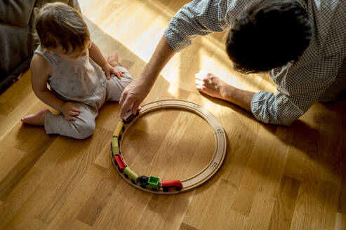 Vater und Sohn spielen mit einer Spielzeugeisenbahn auf einem Hartholzboden zu Hause - ANAF00530