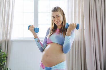 Lächelnde schwangere Frau, die zu Hause mit Hanteln trainiert - MDOF00223