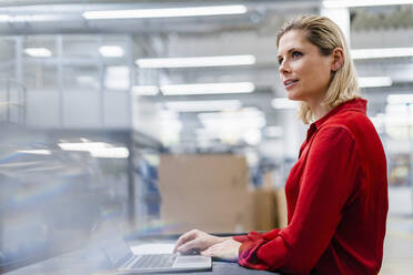 Thoughtful businesswoman with laptop at factory - DIGF19359