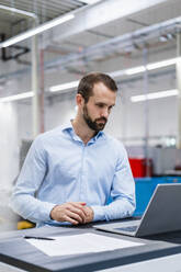 Junger Geschäftsmann mit Laptop in einer Fabrik - DIGF19362