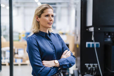 Contemplative businesswoman standing with arms crossed at factory - DIGF19370
