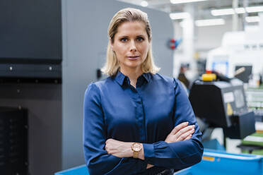 Confident businesswoman wearing blue shirt with arms crossed at factory - DIGF19372