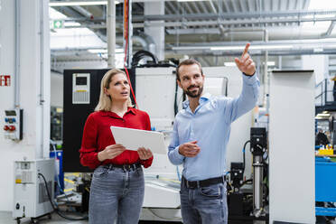 Businessman gesturing by colleague holding tablet PC at factory - DIGF19378