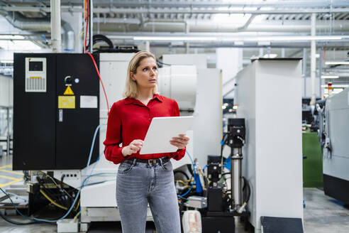 Thoughtful businesswoman with tablet PC standing in factory - DIGF19384