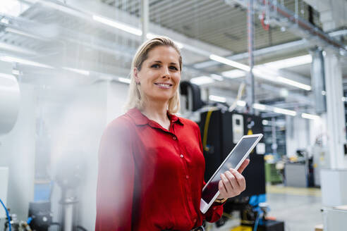 Businesswoman wearing red shirt holding tablet PC in industry - DIGF19388