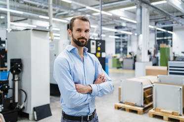 Smiling businessman with arms crossed at factory - DIGF19397