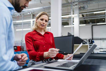 Geschäftsfrau diskutiert mit Kollege über Laptop in Fabrik - DIGF19401