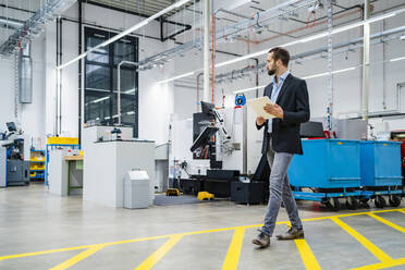 Businessman walking on markings in production hall holding tablet PC at factory - DIGF19434