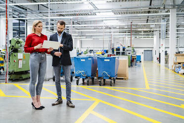 Business colleagues sharing tablet PC standing in production hall at factory - DIGF19435