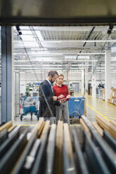 Business colleagues discussing over tablet PC standing in production hall - DIGF19444