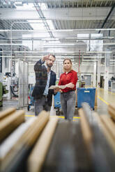 Businessman pointing by colleague standing in production hall in factory - DIGF19445