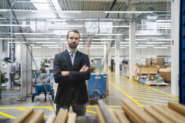 Confident businessman with arms crossed standing in factory - DIGF19449