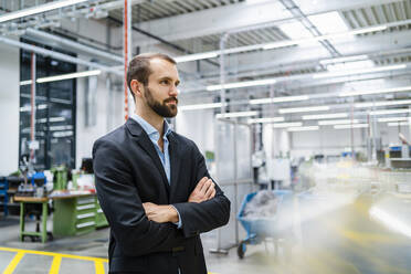 Contemplative businessman with arms crossed standing in factory - DIGF19450